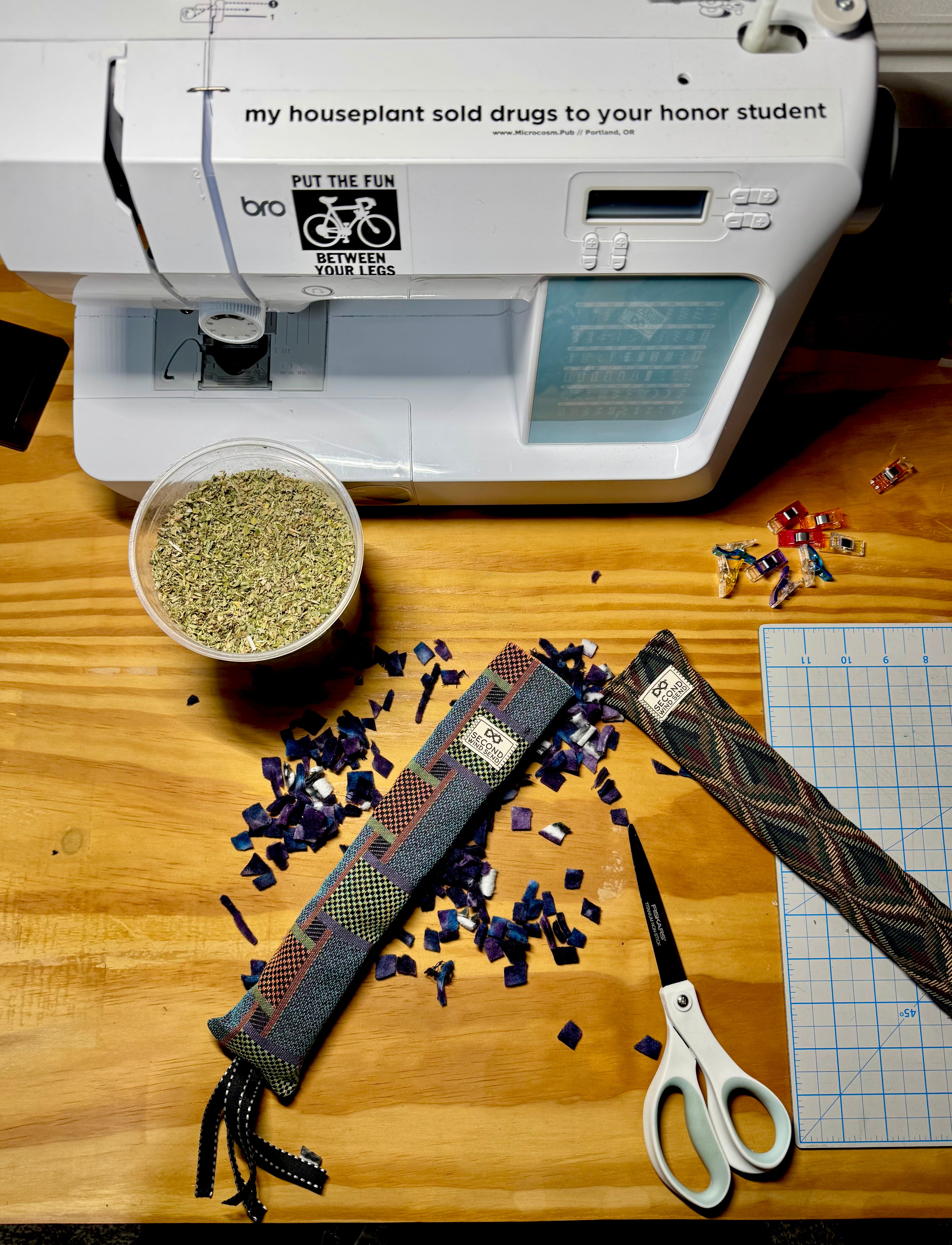 sewing machine on top of table at the top of the image with a container of catnip, clips and scissors and cat kicker toys below it